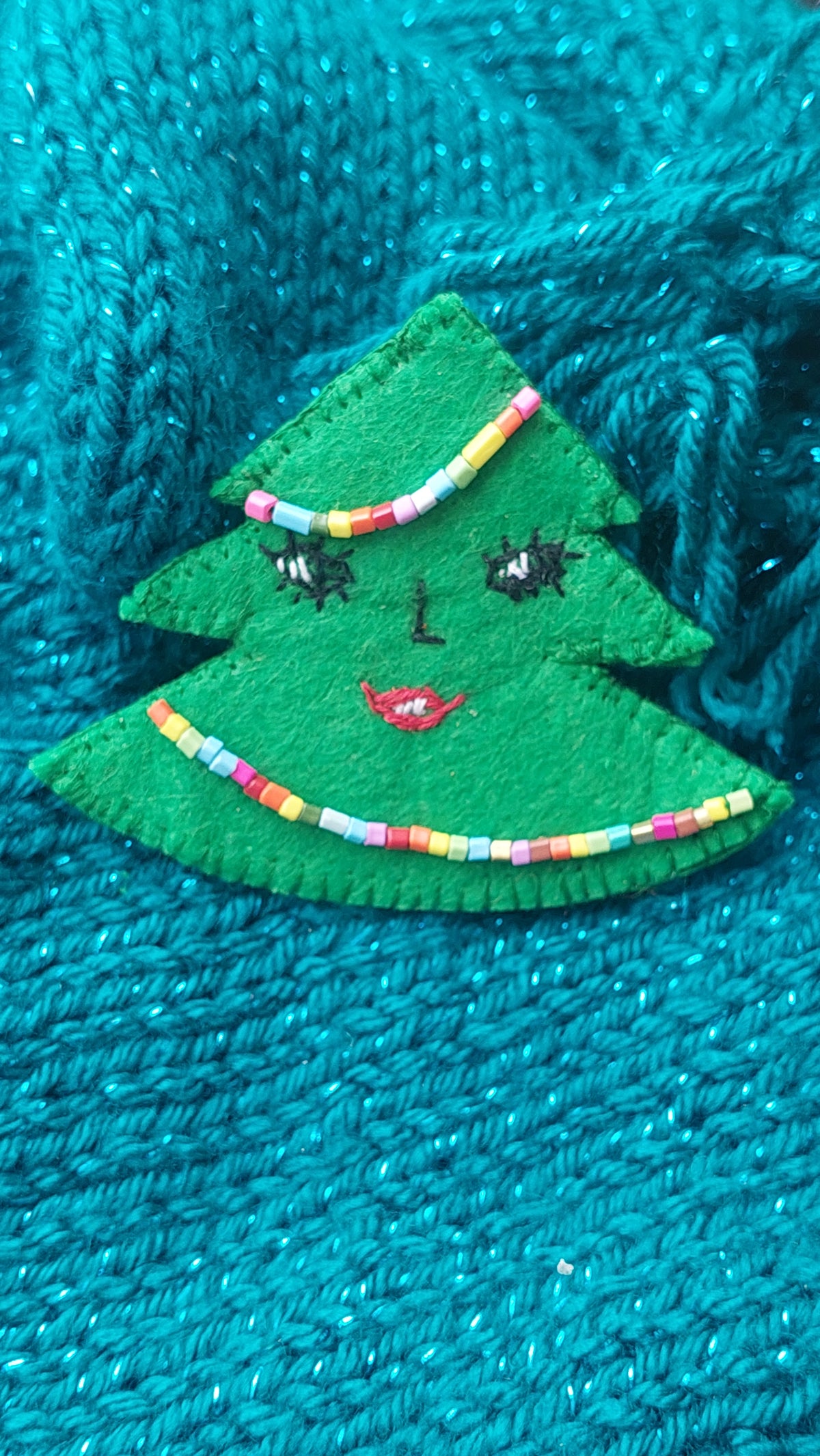 Close-up of colorful beadwork and hand embroidery on a handmade Christmas tree brooch