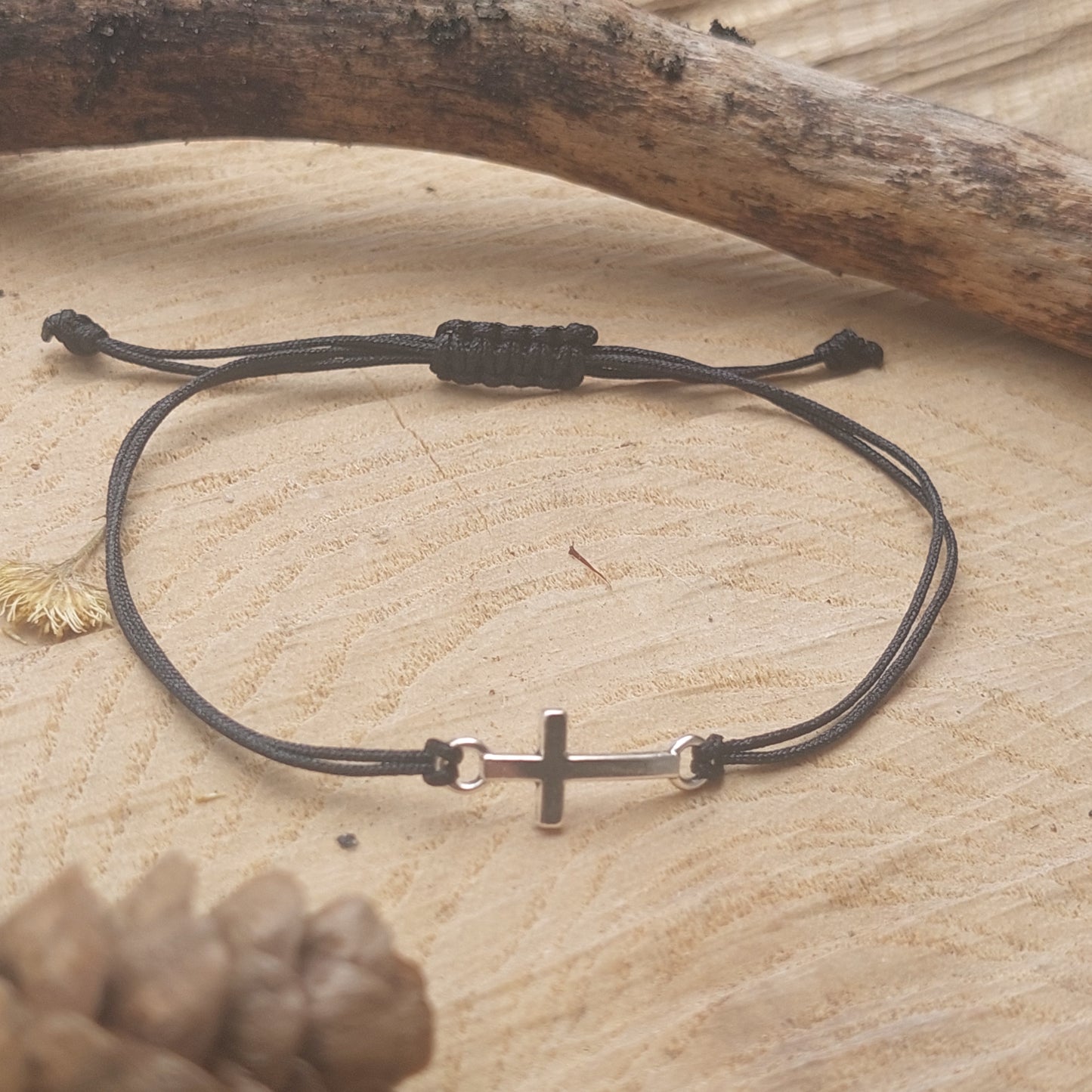 Flat lay of black cord macrame cross bracelet with silver cross – handmade gothic unisex bracelet
