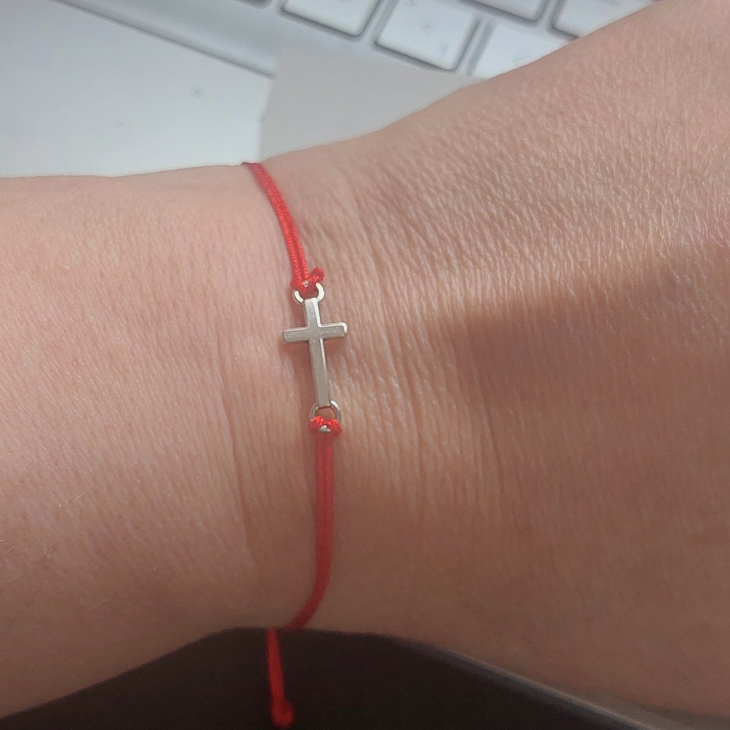 Close-up of silver-tone stainless steel cross charm on red waxed macrame bracelet by Angelenade