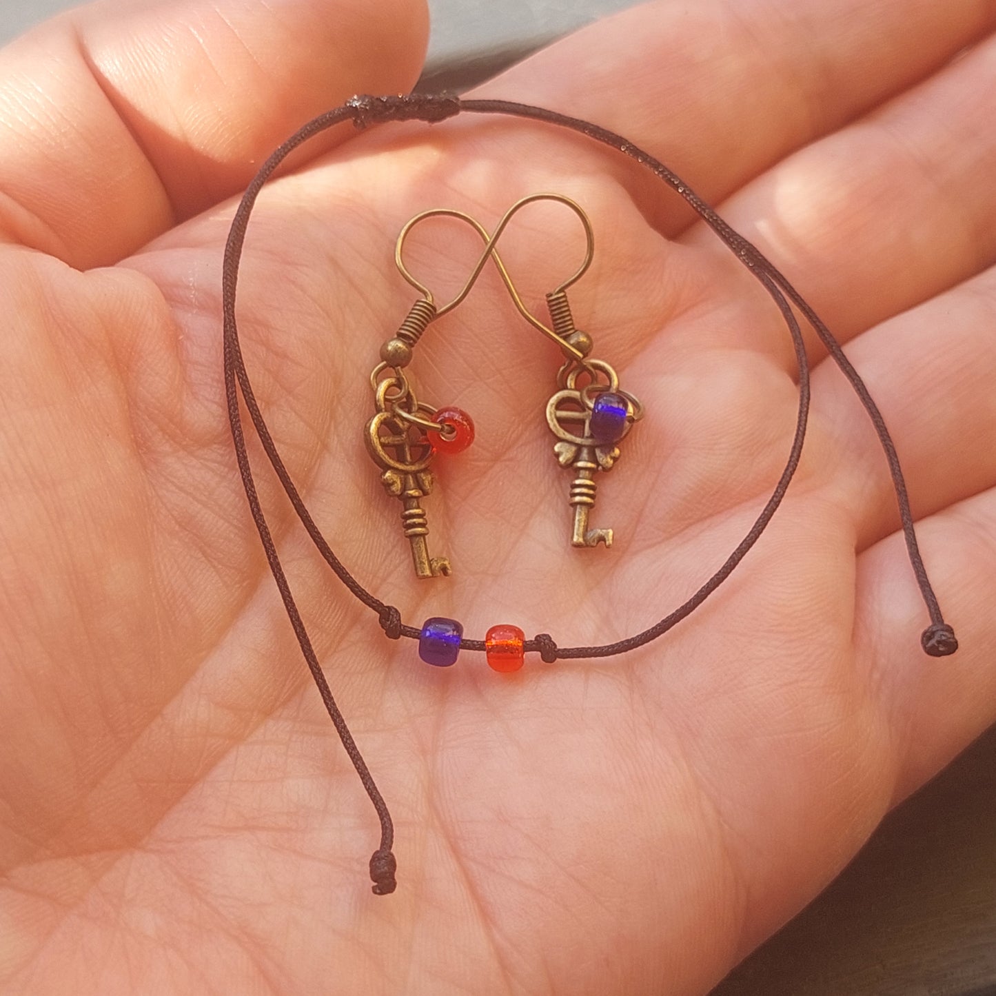 Antique gold key earrings with red and blue beads – Matrix Choice jewelry Antikgold Schlüssel Ohrringe mit roten und blauen Perlen – Matrix Choice Schmuck Minimalist macrame bracelet with red and blue beads – handmade gift Minimalistisches Makramee Armband mit roten und blauen Perlen – handgemachtes Geschenk Matrix Choice jewelry set – earrings and bracelet with symbolic design Matrix Choice Schmuckset – Ohrringe und Armband mit symbolischem Design